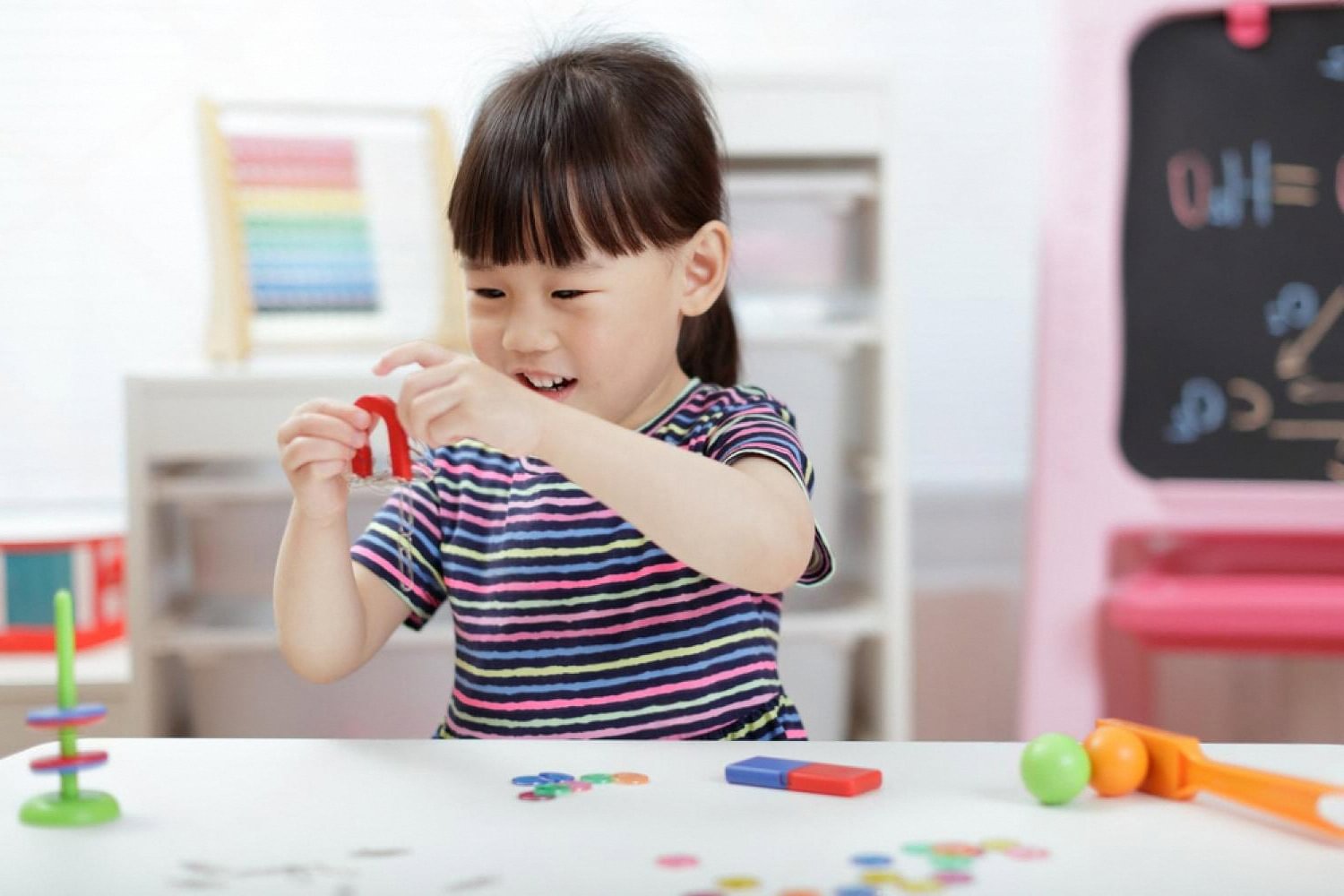 Young girl playing with a colorful learning toy at a desk indoors