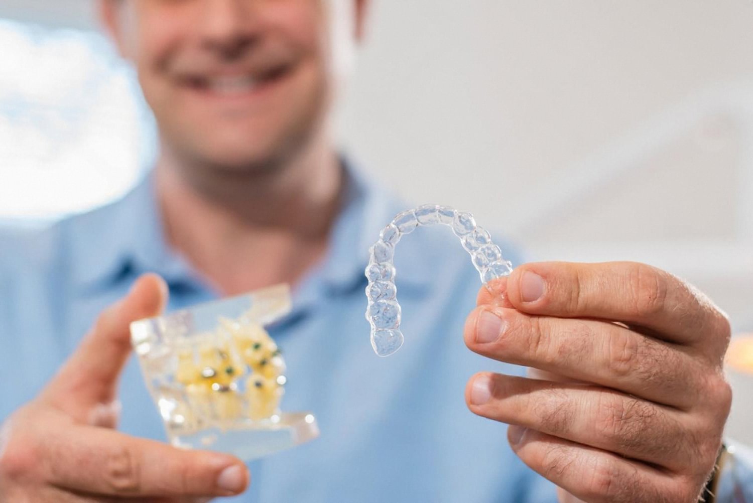 Dentist in Dubai holding an Invisalign clear aligner tray next to a teeth model