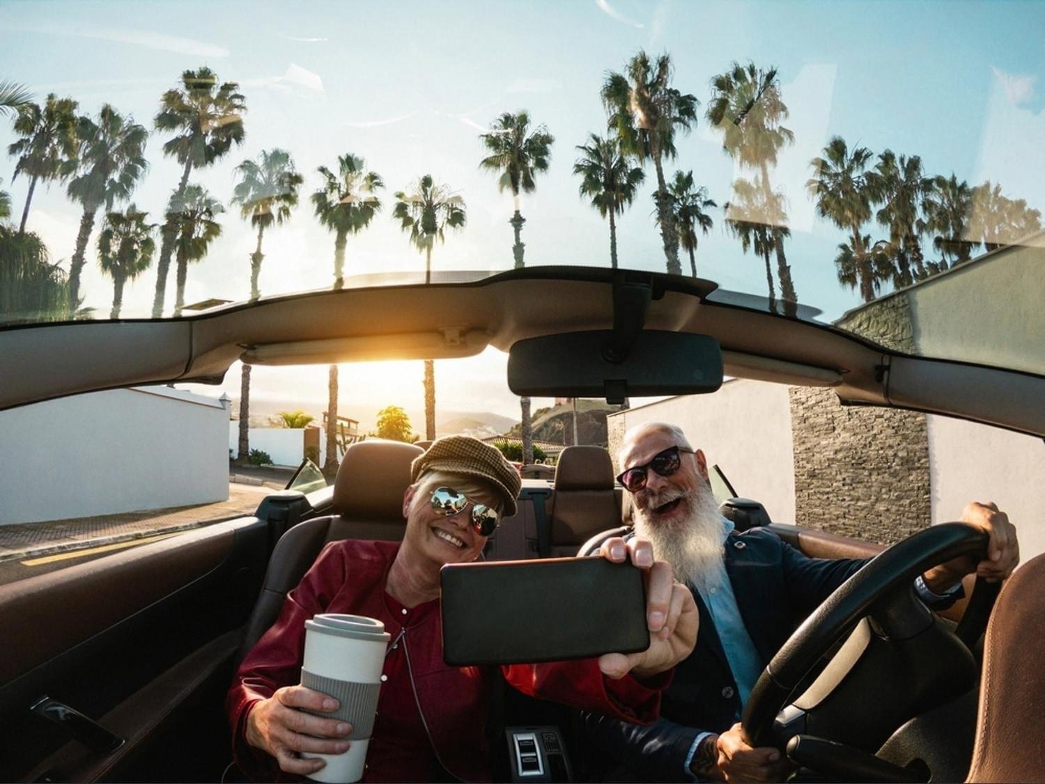 Older couple taking a selfie in a rented convertible on a Dubai palm-lined road